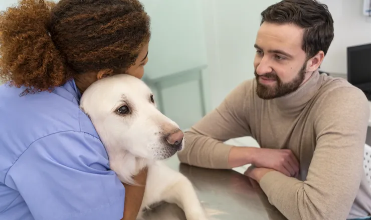 Veterinária abraçando um cão ao lado do tutor
